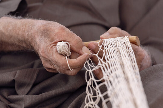 Old man is knitting traditional fishing net, hands in frame. UAE heritage