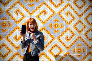Obraz premium Excited woman showcasing smartphone outdoors.