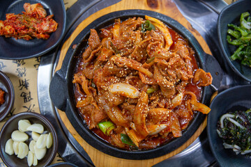 Fototapeta premium Spicy stir fried pork with onions and green onions served on a sizzling hot plate, traditional Korean dish featuring rich red pepper seasoning and savory flavor.