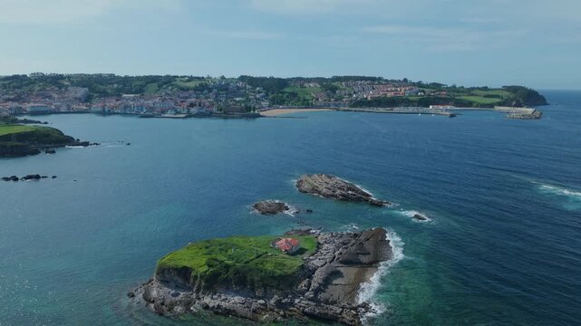 Aerial view flying away from Isla del Carmen revealing the coastal town of Luanco in Asturias, Spain, on a sunny day
