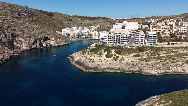Aerial view of Xlendi Bay with turquoise water surrounded by limestone cliffs and white residential buildings Munxar, Gozo Region, Malta.