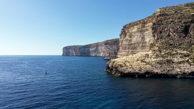 Aerial view of the rugged Xlendi cliffs and deep blue Mediterranean Sea under a clear sky in Munxar, Gozo Region, Malta.