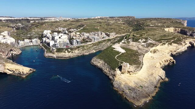 Aerial view of Xlendi Bay featuring the historic watchtower on the rocky cliffs and coastal buildings in Munxar, Gozo Region, Malta.