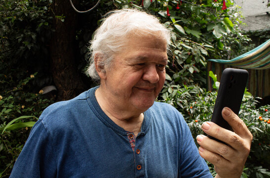 Adulto mayor feliz usando un tel&eacute;fono inteligente al aire libre