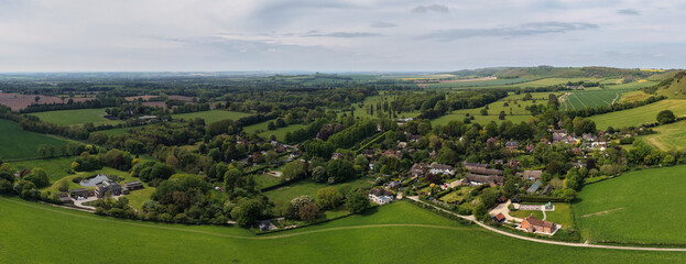 Aerial drone picture of Oare village in Wiltshire, England, showcasing a peaceful rural setting with traditional houses, green fields, and rolling countryside under a sunny sky © Radd