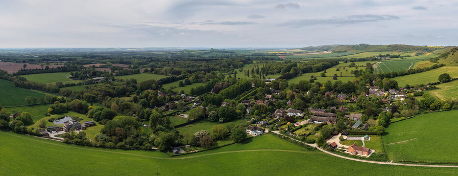 Aerial drone picture of Oare village in Wiltshire, England, showcasing a peaceful rural setting with traditional houses, green fields, and rolling countryside under a sunny sky