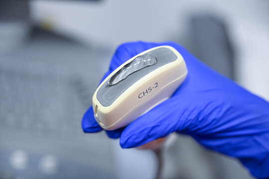 Close up of ultrasound transducer with gel in healthcare professional hand. Sonography, diagnostic imaging and medical examination concept.
