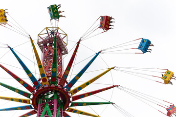 A low-angle shot looking up at a vibrant, multi-colored starflyer or swing carousel ride against a clear sky. © Dina Luk