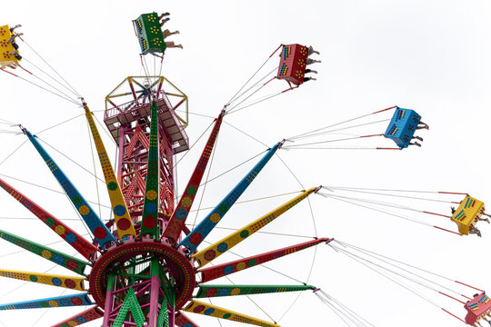 A low-angle shot looking up at a vibrant, multi-colored starflyer or swing carousel ride against a clear sky.