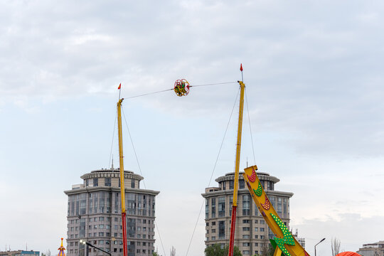 A thrilling reverse bungee ride (slingshot) catapulting passengers high into the sky against the backdrop of modern residential skyscrapers in a city amusement park, Bishkek, Kyrgyzstan.