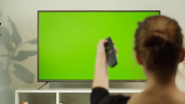 Woman Changing TV Channel with Remote Control and Green Screen Television at Home 4K