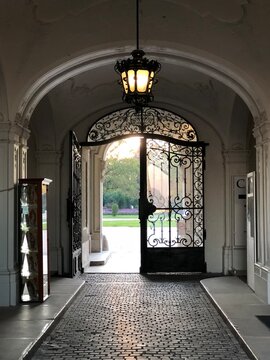 View through an elegant arched stone doorway and an open ornate wrought iron gate leading towards the bright sunny gardens of the historic Festetics Palace in Keszthely, Hungary.