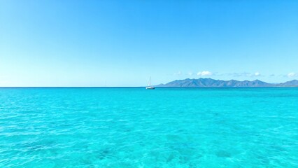 Obraz premium Sunny ocean with sailboat and mountains