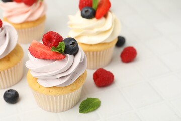 Obraz premium Yummy cupcakes with fresh berries and mint on light tiled table, closeup. Space for text