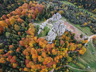 Fototapeta premium Aerial view of rock formation amidst vibrant autumn forest. Landscape features winding pathways and scattered structures, ideal for outdoor activities and exploration. Carpathian mountains, Ukraine.