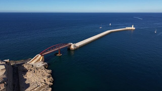 Aerial view of the Saint Elmo lighthouse and red arched bridge extending into the blue Mediterranean sea in Valletta, Port Region, Malta.