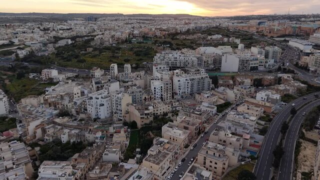 Aerial view of dense residential buildings and winding roads during sunset with a warm sky in Msida, Eastern Region, Malta.