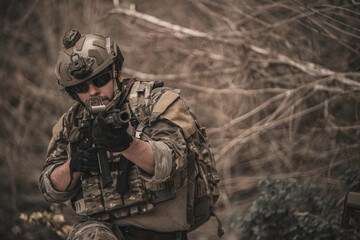 Obraz premium Armed tactical operator aiming rifle during military combat mission in outdoor nature environment. Professional private military contractor conducting security patrol operation in forest wilderness.