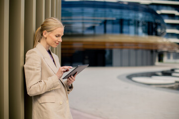 Fototapeta premium Businesswoman uses tablet while standing near modern building in city
