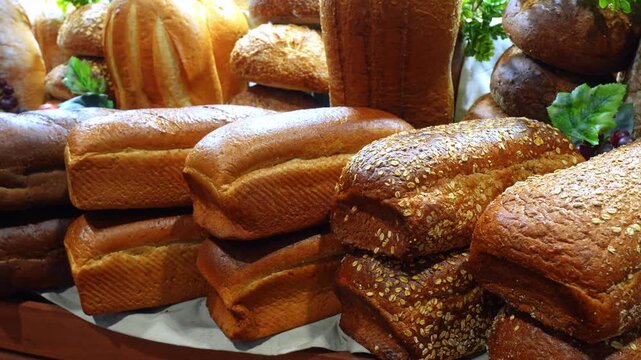Assorted whole grain and rye bread loaves stacked at food show. Dark crusted oat topped loaves with herbs and grapes as garnish.