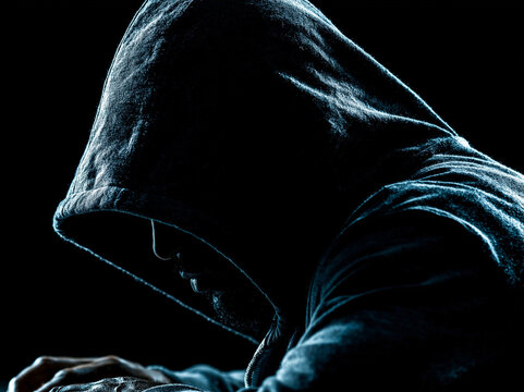 Close up a criminal in black hood , working in the darkness , blak background.