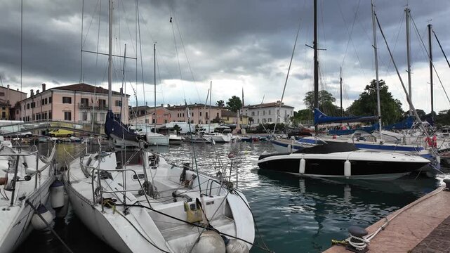 Bardolino, Italy - May 14, 2026 - Sailboats and motorboats docked in a picturesque European harbor under cloudy skies
