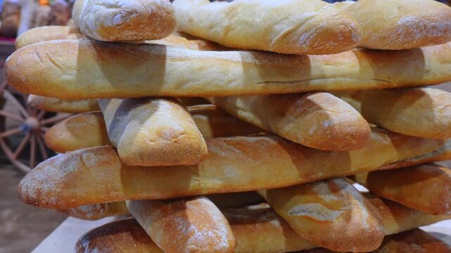 Stacked French baguettes dusted with flour at bakery display. Close up of layered crusty loaves with golden brown surface and soft texture.