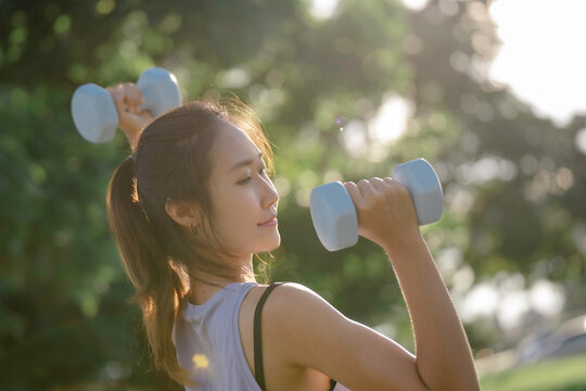A woman is lifting dumbbells in a park and exercising.