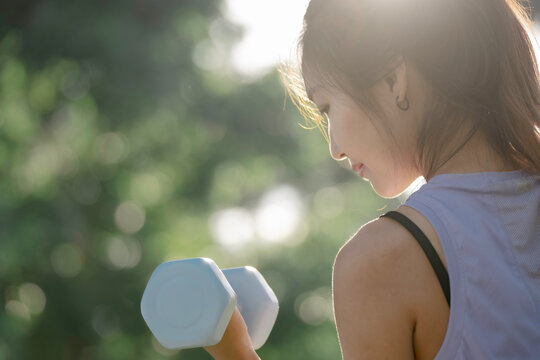 A woman is lifting dumbbells in a park and exercising.
