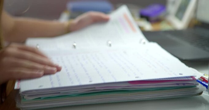 Document Review: A person's hands delicately turn the pages of a thick, paper-bound notebook filled with handwritten notes and diagrams, suggesting focused study or meticulous record-keeping.