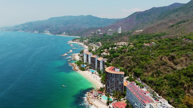 Aerial view of Las Gemelas Beach with high-rise resorts, turquoise ocean water, and lush green mountains in Puerto Vallarta, Jalisco, Mexico.