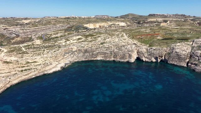 Aerial view of Dwejra Bay featuring deep blue waters surrounded by rugged limestone cliffs and arid coastal landscape in Gozo region, Malta.