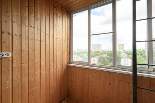 Wood-paneled balcony with vertical clapboard walls, large multi-pane windows, a visible electrical outlet, and a view of the cityscape with buildings and greenery