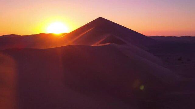 A beautiful sunset over the desert and mountains fills the orange sky with light as the sun dips behind the distant hills