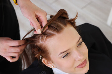 Fototapeta premium Hairstylist braiding teenage girl's hair in salon, closeup