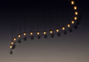 Naklejka premium Decorative string of glowing vintage light bulbs hanging in darkness