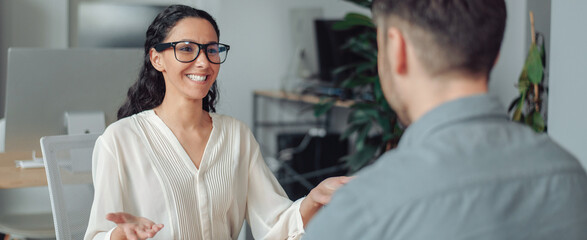 Fototapeta premium Smiling Hispanic Woman Engaging In Conversation With A Male Colleague At Office Setting, Expressing Friendly Gesture While Discussing Ideas Or Projects. Business Concept