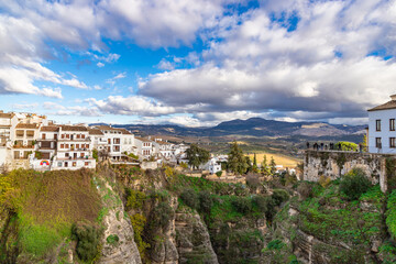 Obraz premium RONDA, SPAIN - DECEMBER 17, 2025: High angle panoramic view of the lush El Tajo gorge in Ronda with white houses and historic architecture perched on steep limestone cliffs.