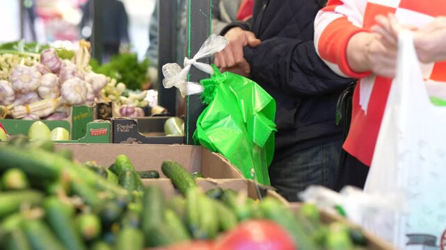 Fresh green cucumbers and garlic on display at an outdoor marketplace stall with customers shopping representing local retail trade and agricultural commerce