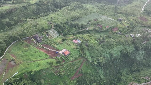 Aerial view of Joglo Java Neglasari villas nestled among lush green hills and terraced fields in Cigombong, West Java, Indonesia.