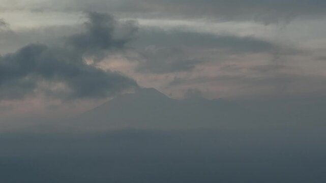 Aerial view of a mountain peak shrouded in thick grey clouds and mist during a moody dawn in Cigombong, West Java, Indonesia.