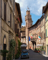 Naklejka premium Walking down a narrow street in Tuscany, Italy, with a clock tower in view and flags hanging from buildings