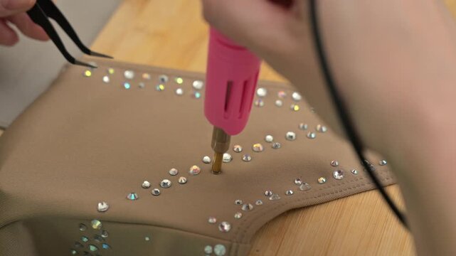 A woman glues rhinestones onto a gymnastics costume using a soldering iron. Hot fix.