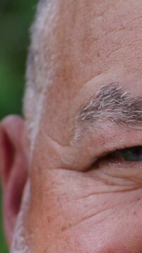 Vertical video: Camera showing senior man opening right eye, shifting gaze outside, green iris seen