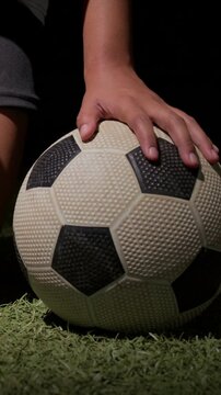 Vertical video: Placing player hand moving grip on ball on turf, shorts visible preparing kick