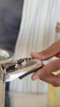 Vertical video: Hand pressing button, lifting latch and stirring pot on stove, venting steam, apron