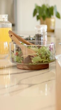 Vertical video: Aligning glasses, arm in light top reaching across kitchen by salad bowl to serve