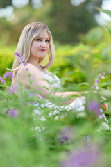 Obraz premium Woman seated among green plants and purple flowers