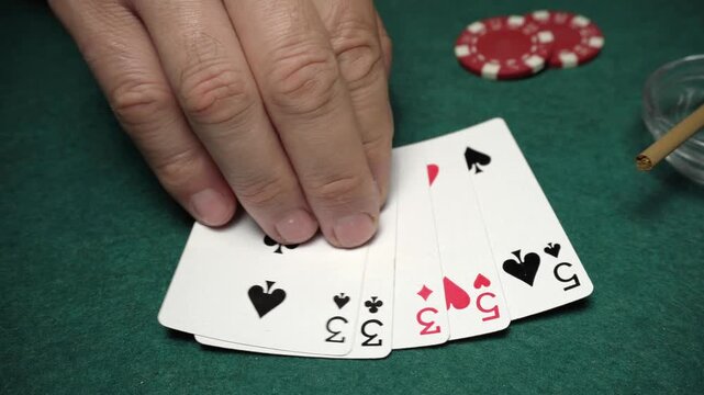Hand places playing cards on a green felt poker table with poker chips and a cigarette visible in the background