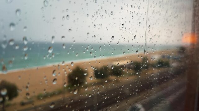 Gotas de lluvia sobre una ventana con playa y costa mediterr&aacute;nea desenfocadas al fondo &mdash; v&iacute;deo 4K